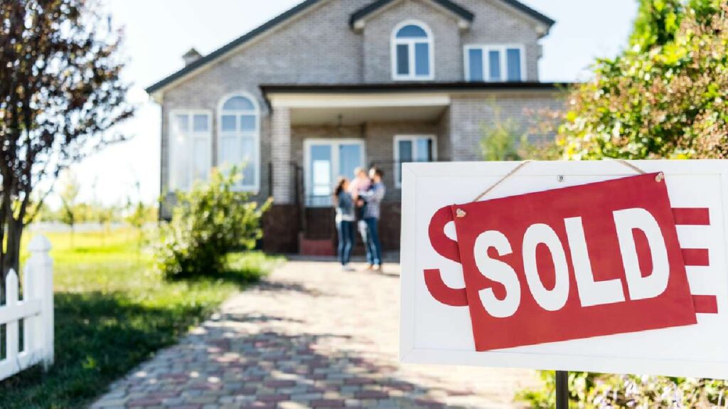 Do you know the signs your house will sell fast? this happy family is standing proudly in front of their sold home, with a 'For Sale' sign featuring a 'Sold' sticker, indicating signs that their house sold fast.